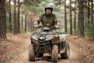 Homme adulte équipé d'un casque intégral et d'une veste de protection conduisant un quad sur un chemin forestier en terre
