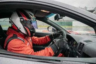 Pilote en combinaison de course au volant d'une voiture de sport sous la pluie lors d'un stage de pilotage sur circuit